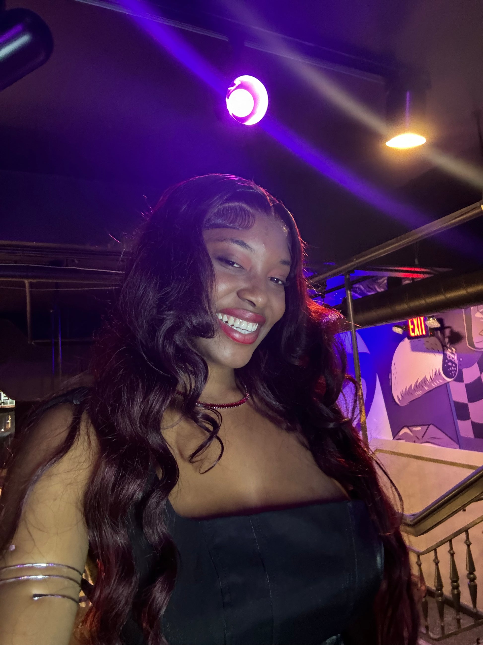 Woman with long hair smiling in a dimly lit room with purple lighting